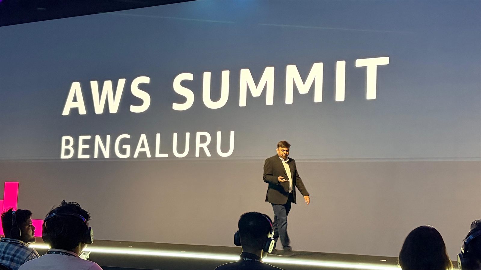 Prashant Akhawat walking the stage in front of the AWS Summit Bengaluru title wall.
